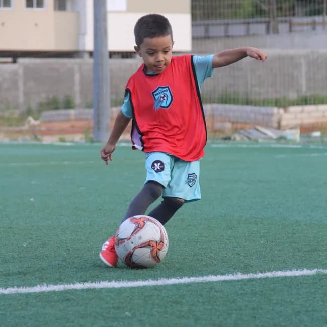 Aluno da escolinha conduzindo a bola na grama sintética
